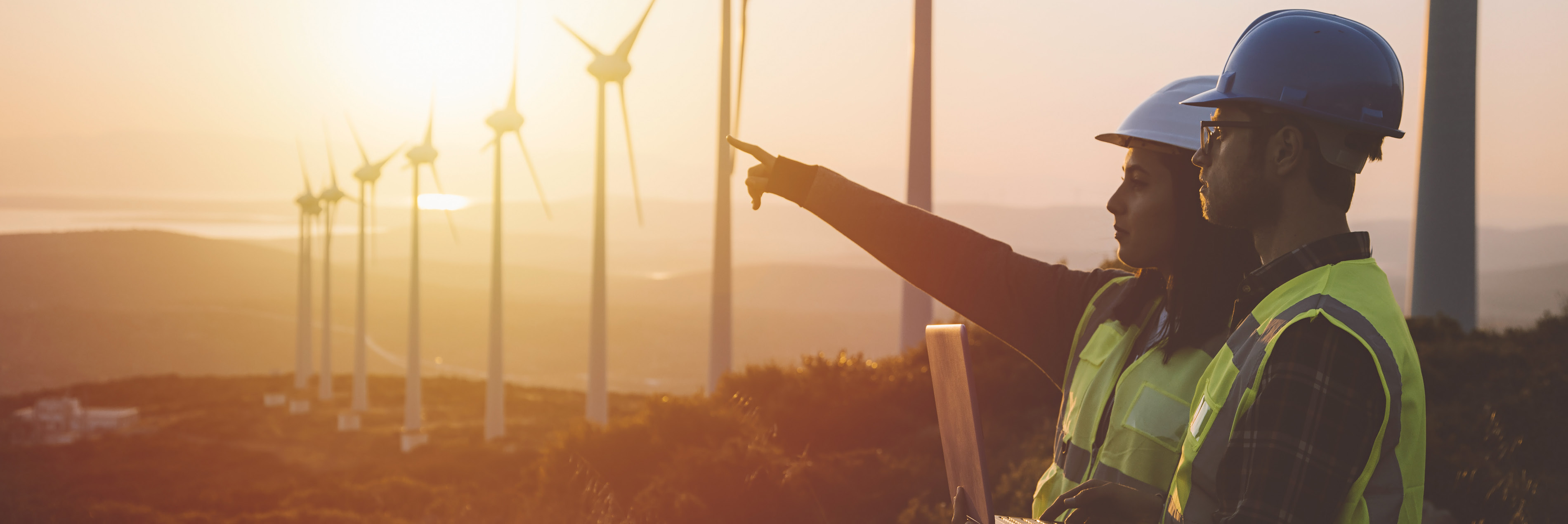 Photo of a man and woman standing together with wind turbines in the background