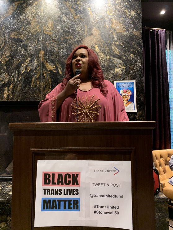 Person speaking in front of a Black Trans Lives Matter sign